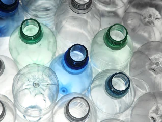 Overhead close-up: Empty, clear plastic bottles (caps removed, some green/blue tint) emphasizing plastic recycling.