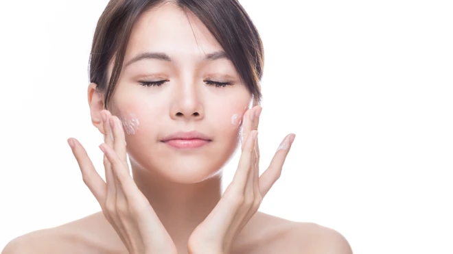 East Asian woman applying skincare to her face