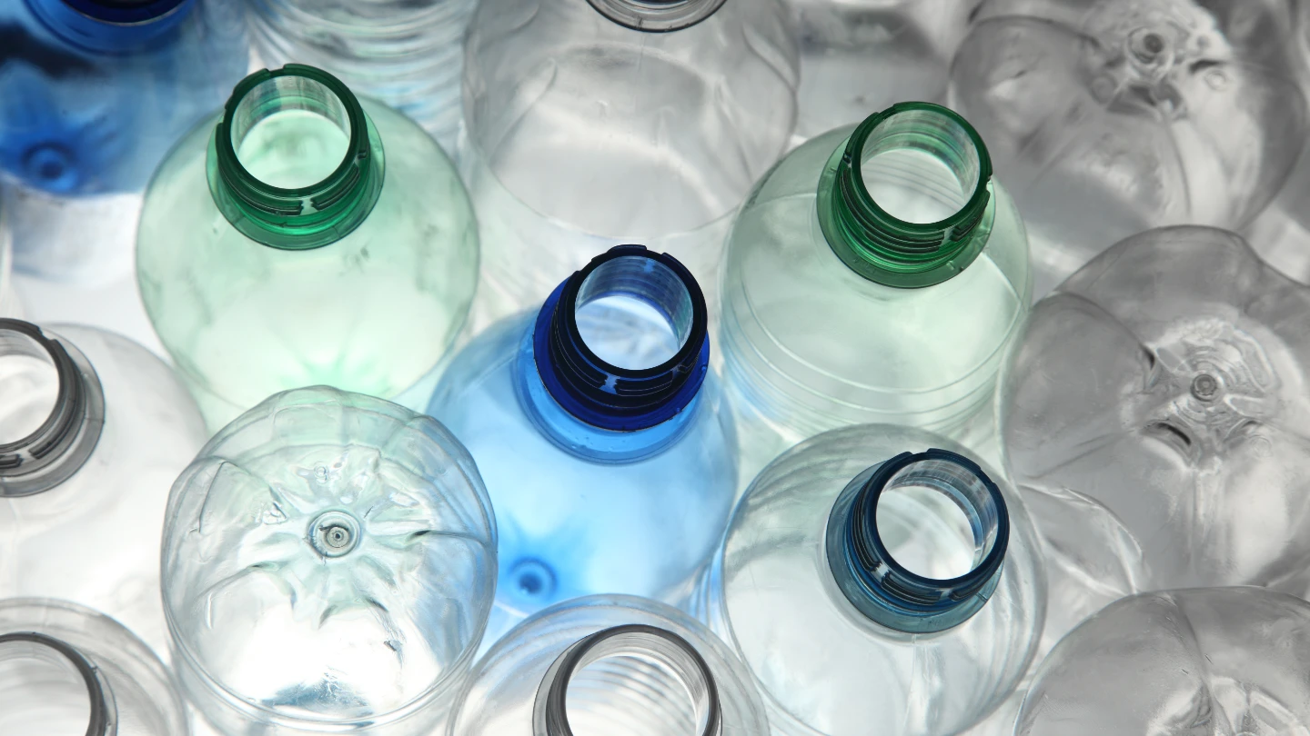 Overhead close-up: Empty, clear plastic bottles (caps removed, some green/blue tint) emphasizing plastic recycling.