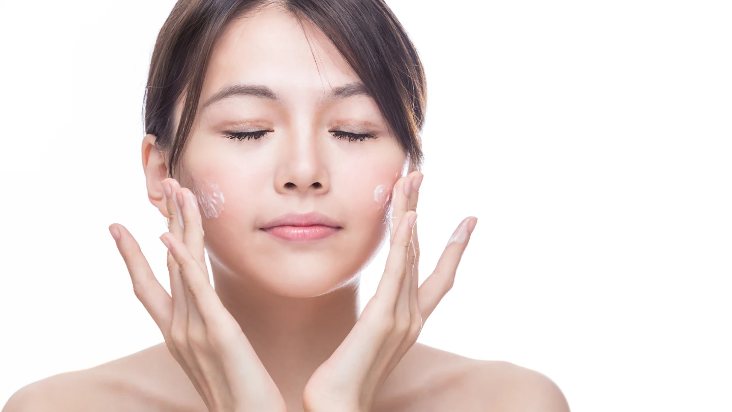 East Asian woman applying skincare to her face