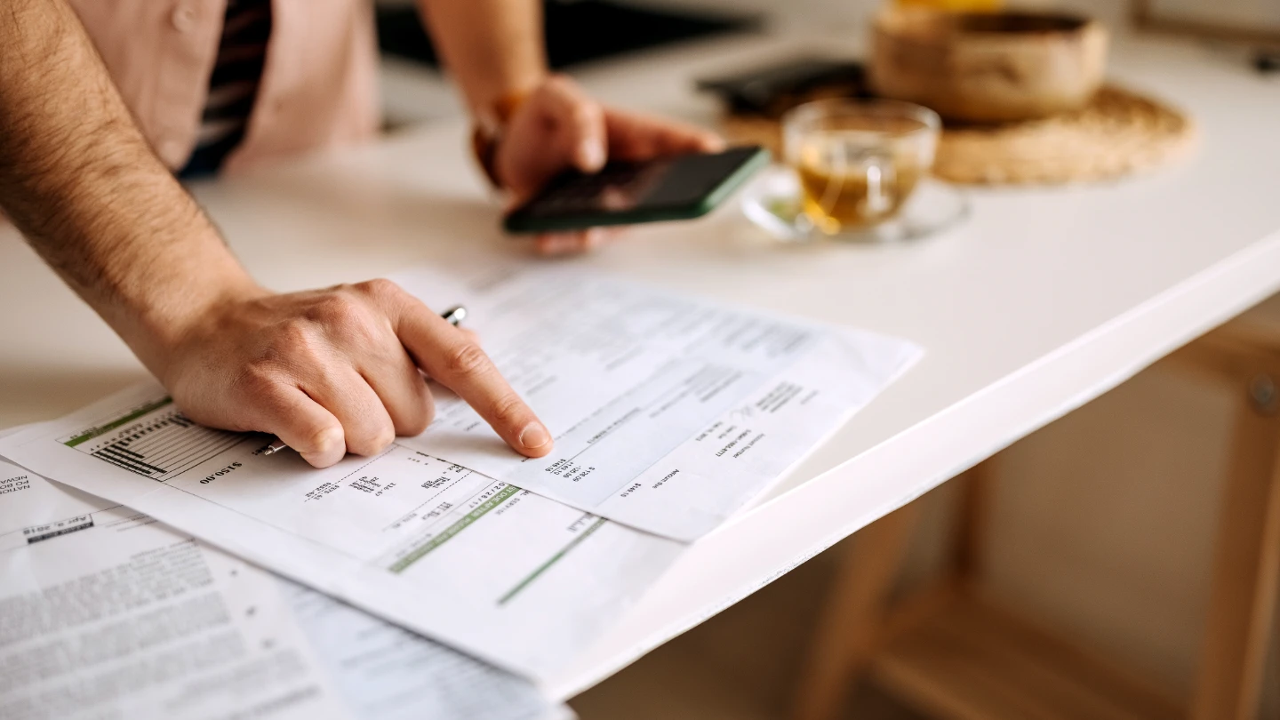 man pointing at sheet and holding mobile phone